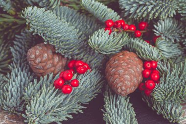 Yeni yıl. Noel kompozisyonu. Kırmızı böğürtlenli dallar, beyaz ahşap arka planda koniler. Pastel renkler