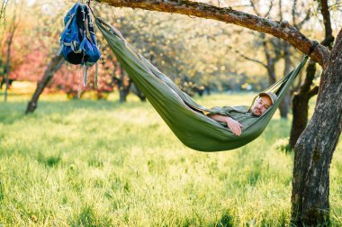Mutlu traveler sakallı hipster yaz güneşli gün tatil turuncu çiçek açan bahçede elma ağacı üzerinde yatan yeşil şapkalı adam. Hafta sonu ve tatil. Turizm. Boş zaman. Rüya. Koku havada.