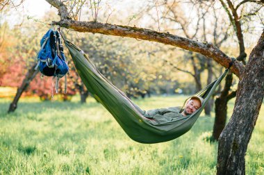 Mutlu traveler sakallı hipster yaz güneşli gün tatil turuncu çiçek açan bahçede elma ağacı üzerinde yatan yeşil şapkalı adam. Hafta sonu ve tatil. Turizm. Boş zaman. Rüya. Koku havada.