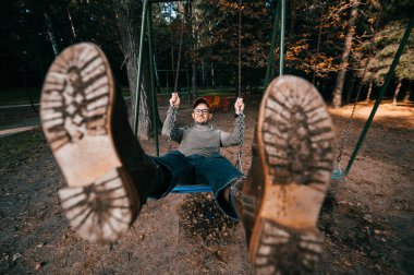 Garip, tuhaf, tuhaf insanlar konsepti. Çocuk parkında salıncakta sallanan pahalı, modaya uygun botları olan yetişkin bir adam. Çok komik bir fikir. Çocuk içeride. Bacaklarını aç.. 