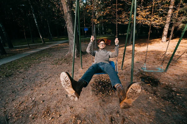 Odd bizarre eccentric people concept. Adult man in vintage expensive fashionable boots riding on a swing in city park on playground for children. Crazy funny idea. Child inside. Legs spread wide. — Stock Photo, Image