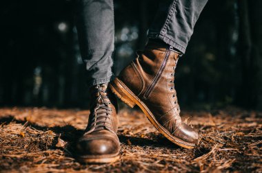 Kaliteli hippi erkeksi, kaba deri, tahta çizmeli tuhaf oduncu. Sonbahar ormanında yerde kuru turuncu ladin iğneleriyle dikiliyor. Sonbahar renkleri ve ruh hali konsepti. Hafta sonu güneşli bir gün..