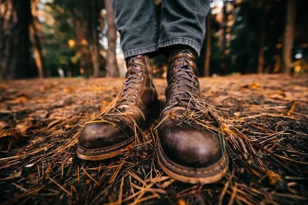 Man 's benen in houthakker vintage lederen laarzen en bijgesneden jeans staan in de herfst bos op de grond. Herfst kleuren en stemming concept. Comfortabele schoenen. Wandelen in het weekend op de natuur. Verstoring van de lens. — Stockfoto
