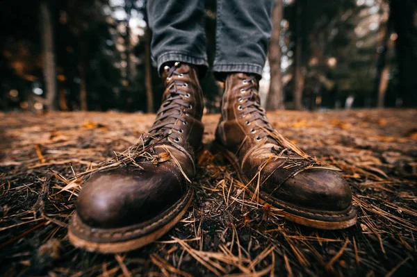 Männerbeine in Holzfällerlederstiefeln und zerschnittenen Jeans stehen im herbstlichen Wald auf dem Boden. Herbstfarben und Stimmungskonzept. Bequeme Schuhe. Wandern am Wochenende in der Natur. Linsenverzerrung. — Stockfoto