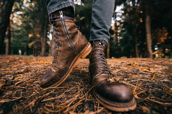 Ağaç kesen, deri çizmeli ve kırpık kotlu bir adam sonbahar ormanında yerde duruyor. Sonbahar renkleri ve ruh hali konsepti. Rahat ayakkabılar. Hafta sonu doğa yürüyüşü. Mercek bozulması. 