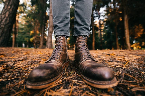 Pernas de homem em botas de couro vintage cortador de madeira e jeans cortados de pé na floresta de outono no chão. Cores de queda e conceito de humor. Sapatos confortáveis. Caminhando no fim de semana na natureza. Distorção da lente. — Fotografia de Stock