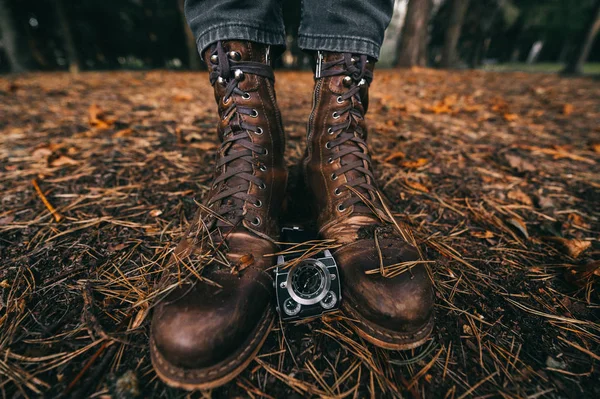 Botas y relojes en el suelo en el bosque de otoño con agujas de abeto, hojas y conos de pino. Viejo calzado hipster vintage. Concepto masculino. Estaciones y tiempo. — Foto de Stock