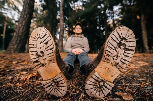Odd weird woodcutter sitting in autumn forest on ground. Take a rest. Lunch brake on nature. Wooden sole. Wet and raw fall. Fresh air outdoor. Trees on background. Colors of seasons. Lens distortion. — Stock Photo, Image