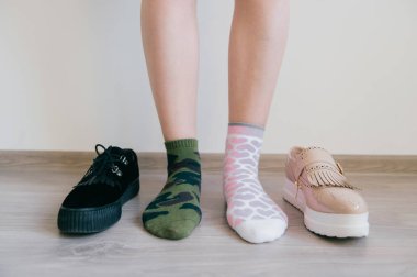 Çıplak kadın bacakları yerde duruyor. Uyumsuz pamuklu çoraplı kadın ayakları. Garip, alışılmadık, tuhaf, tanınamaz, tuhaf, tuhaf kız. Acımasızlık ve şefkat kavramı. Farklı büyük bir ayakkabı seçimi.. 