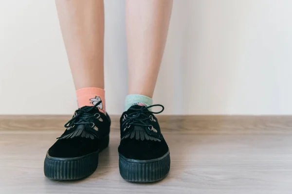 Pies femeninos en negro elegante zapatos de gamuza negro femenino con tanqueta. Las piernas de las mujeres en calcetines de algodón desiguales. Piel suave bronceada. Inusual inatento irreconocible chica de pie en el suelo en casa. — Foto de Stock