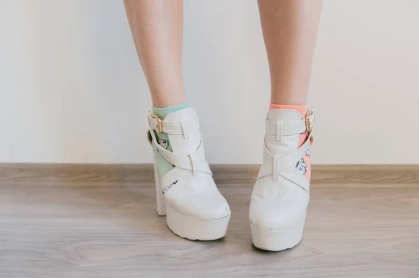 Kinky kvinnors ben i missmatched färgglada bomullsstrumpor på vit bakgrund. Kvinnliga fötter i excentriska vitt läder fashionabla trend moderna skor på höga klackar. Oigenkännlig näsvisa kaxig tonåring — Stockfoto