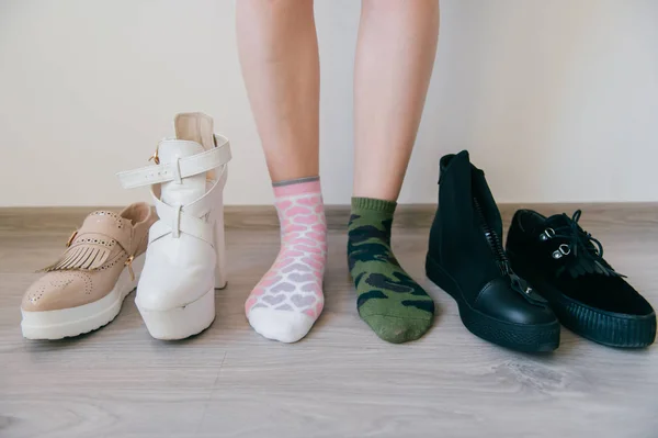 Female naked legs standing on floor. Women`s feet in missmatched cotton socks. Odd unusual weird unrecognizable bizarre kinky girl. Brutal and tenderness concept. Different big choice of footwear.