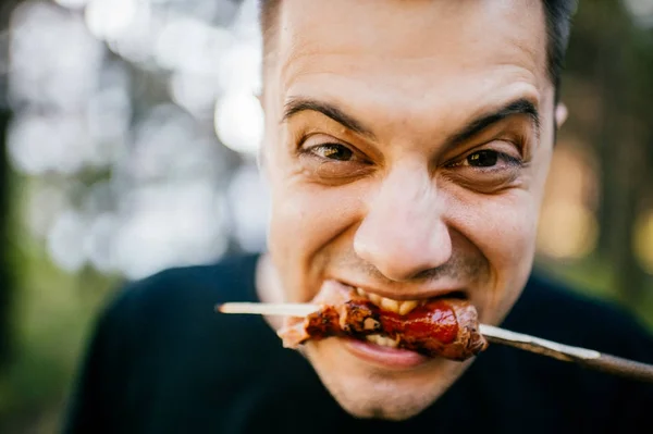 Facial expression of man eating with disgust grilled sausage outdoor. Vegetarian feeling pain and suffering trying meat. Pork is bad. Recycled dead animal. Tasteless fried food. Adult male biting.