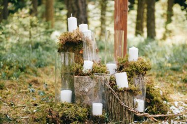 Wedding wooden arch for marriage ceremony with flowers, curtain and other decoration elements standing on ground in forest. Pine trees in sunny summer day. Celebration mood. Candles in glass, feathers clipart