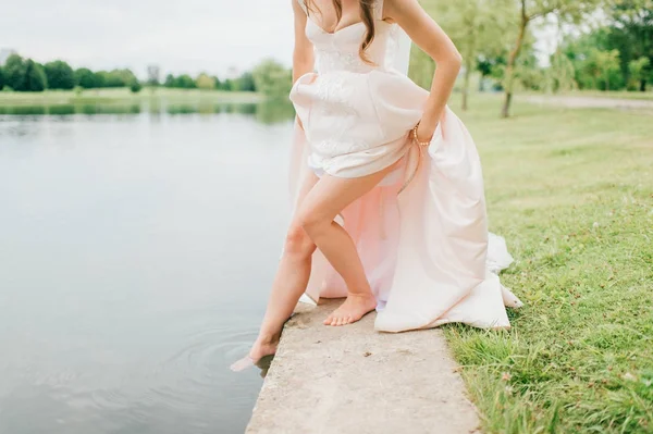 Αγνώριστος νύφη σε ακριβά κομψό νυφικό που πιέζει το slim γυμνή όμορφη πόδι στο ποτάμι. Περίεργη γυναίκα παίζει με νερό εξωτερική. Ηλιόλουστη μέρα θερμό καλοκαίρι. Refelcted άγνωστη κοπέλα στη λίμνη. — Φωτογραφία Αρχείου
