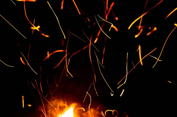 黒い背景に火が火花を散らし、炎が動きます。テクスチャと噴火 — ストック写真