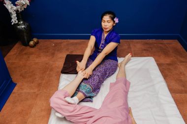 Genç Tay masör işçi kız etnik Asya egzotik kostüm yapar ve mavi gevşeme yoga odasında pembe pijama beyaz güzel bayan için farklı geleneksel spa prosedürler öğeleri gösterir.