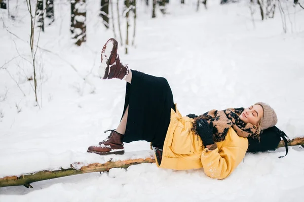 Zvláštní bizarní samice ležící na stromě ve sněhobílém zimním lese. Krásná mladá krásná dívka relaxační venku. Neobvyklá žena na dovolené odpočívající v přírodě. Osamělá dáma cestuje v mrazivém chladném dni. — Stock fotografie