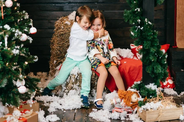 Fiú és lány szerelmes. Karácsonyfa és az új évet dekorációt. Szép kis gyerekek egymást átölelve. Téli ünnepek. Fiatal férfi és női játék, és nevetve a stúdióban. Gyermekek örömteli érzelmeket. — Stock Fotó