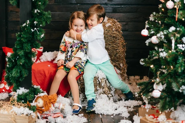 Fiú és lány szerelmes. Karácsonyfa és az új évet dekorációt. Szép kis gyerekek egymást átölelve. Téli ünnepek. Fiatal férfi és női játék, és nevetve a stúdióban. Gyermekek örömteli érzelmeket. — Stock Fotó