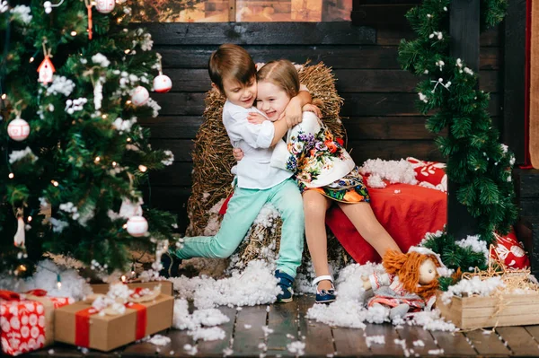 Boy and girl in love. Christmas tree and new year decorations. Lovely little kids hugging each other. Winter holidays. Young male and female playing and laughing in studio. Children joyful emotions. — Stock Photo, Image
