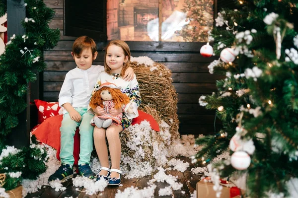 Fiú és lány szerelmes. Karácsonyfa és az új évet dekorációt. Szép kis gyerekek egymást átölelve. Téli ünnepek. Fiatal férfi és női játék, és nevetve a stúdióban. Gyermekek örömteli érzelmeket. — Stock Fotó