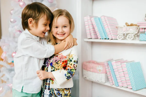 Encantadores niños divertidos se enamoran. Niños abrazándose. Chico guapo abrazando tímido linda niña. Emociones alegres expresivas. Bolas de año nuevo en el árbol de Navidad. Jóvenes amigos y amigas. Relación —  Fotos de Stock