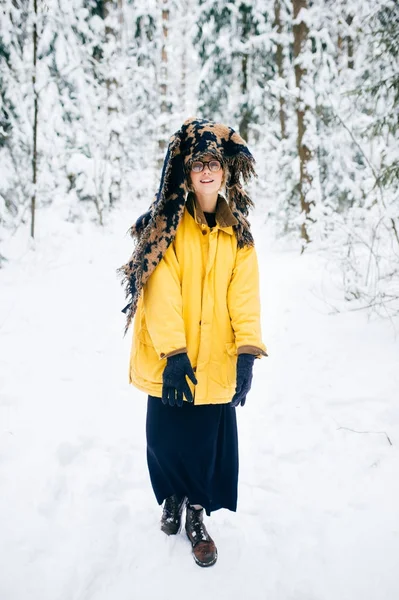 Odd strange young bizarre fancy lonely girl making weird poses in winter snowy forest on weekend. Fashionable mad kinky woman in glasses and warm trendy clothes relaxing outdoor. Crazy headdress.