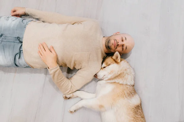 Adult bald man with husky puppy sleeping on floor. Owner with pe — Stock Photo, Image