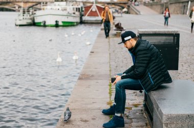 Yalnız adam depresyon bankta oturmuş ve yaşam sorunları düşünüyor. Soyut şehir arka plan. Setin Nehri Prag yürüyüş güvercin. Psikolojik erkek portre. Yalnızlık ve yalnızlık.