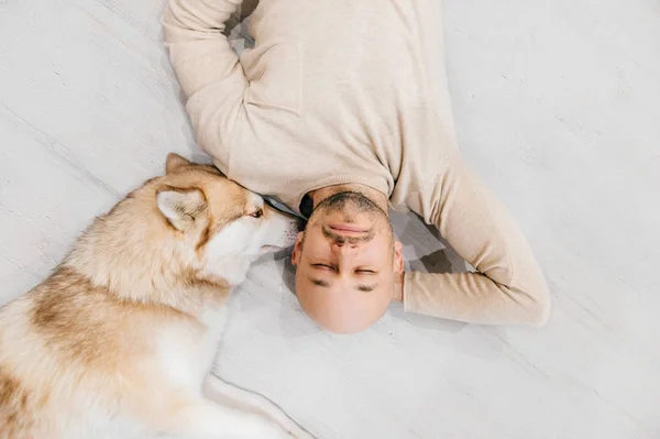 Adult bald man with husky puppy sleeping on floor. Owner with pet together at home. Kind and soulful emotions. Lovely dog resting with young male. Guy with beloved domestic animal hugging each other.