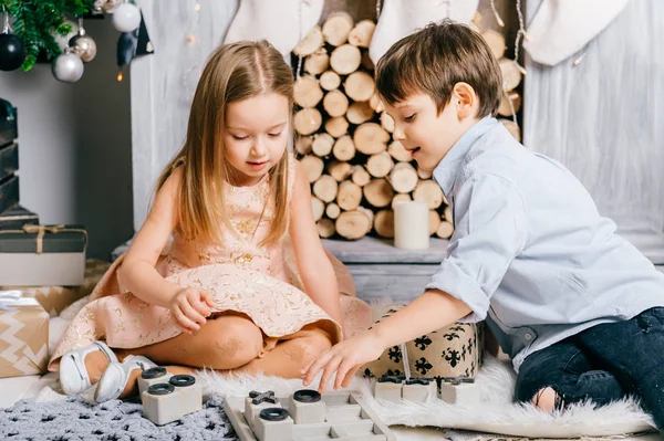 Niños jugando en la habitación interior de año nuevo. Árbol de Crhistmas con bolas. Vacaciones de invierno. Niños felices disfrutando de juguetes. Amigos jóvenes sentados y bromeando. Chico y chica juntos. Celebrando la fiesta . —  Fotos de Stock