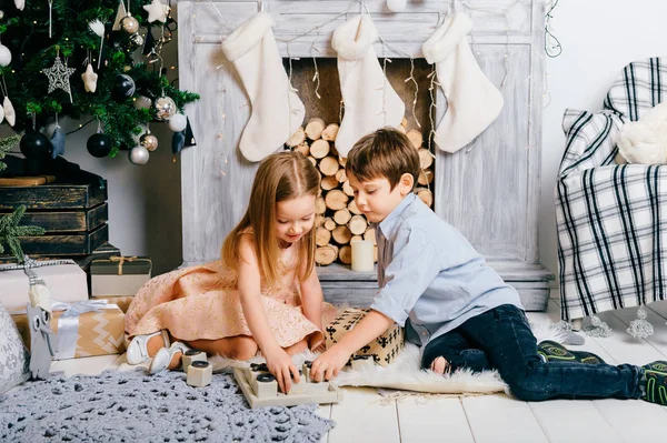 Kinderen spelen op Nieuwjaar interieur kamer. Crhistmas boom met ballen. Winter vakantie stemming. Gelukkige jonge geitjes genieten van speelgoed. Jonge vrienden zitten en een grapje. Jongen en meisje samen. Feest vieren. — Stockfoto