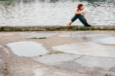 Setin açık kenarında oturan çıplak ayakla yalnız bilinmeyen yetişkin adam. Zavallı evsiz depresyon. Yardım bekliyor. Sorunlu hayat. Psikolojik dramatik erkek portre. Arkadaşı olmayan kişi
