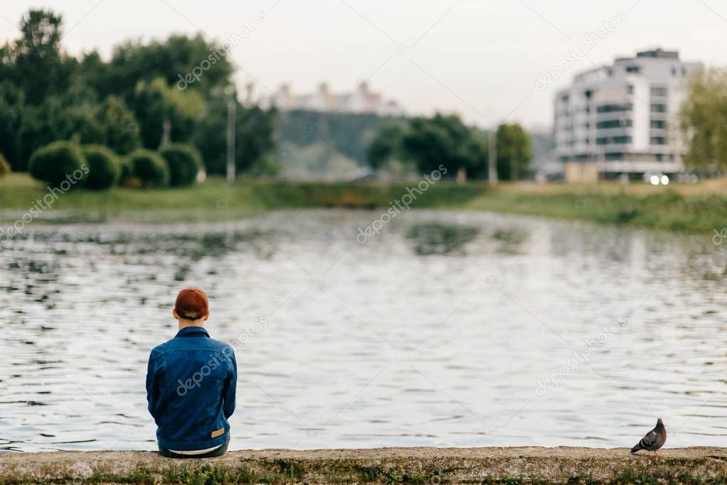 Lonely unrecognizable adult man sitting on edge of embankment in Russia. Homeless poor person in depression. Guy and dove friends. Bird family. Portrait of divorced male from behind outdoor. Solitude