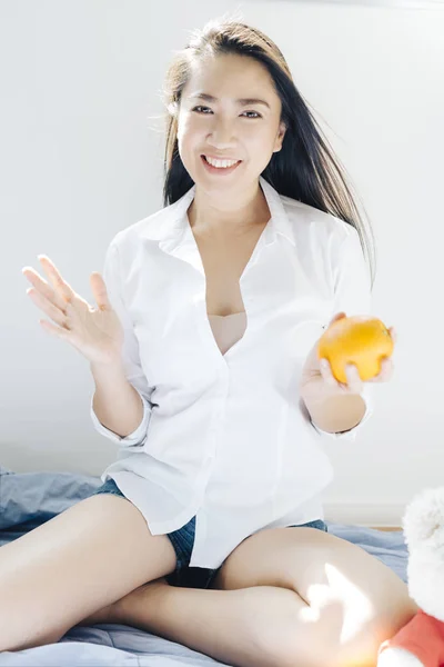 Obstserie: Glückliche Asiatin mit Orange im Schlafzimmer — Stockfoto