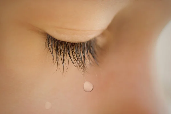 El niño con los párpados cerrados se cierra con una lágrima en las pestañas. Una lágrima corre por su mejilla. El bebé está llorando. — Foto de Stock