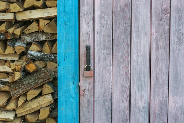 La puerta del viejo granero con pintura blanca. Cerca yacía la madera apilada en una pila. Puerta cerrada en la cerradura . —  Fotos de Stock