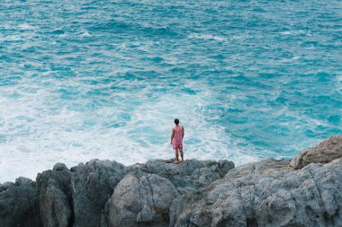 Genç adam kolunu havada deniz cliff üzerinde duran ve manzarasının tadını çıkarın