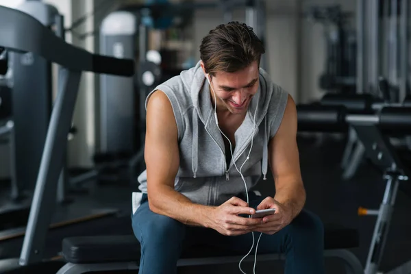 在健身房，短信中使用智能手机的健康健美男子 — 图库照片