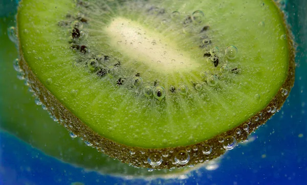 Kiwi e bolhas em um copo em fundo azul — Fotografia de Stock