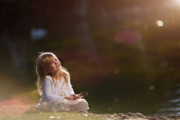 Malá holčička s perem v ruce sedí na trávě za slunečného dne — Stock fotografie