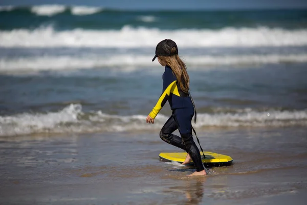 Menina feliz - jovem surfista com bodyboard se diverte na praia de areia do mar com ondas. Estilo de vida familiar, pessoas aulas de esporte aquático, atividade de natação no acampamento de surf de verão férias com criança na ilha oceânica . — Fotografia de Stock