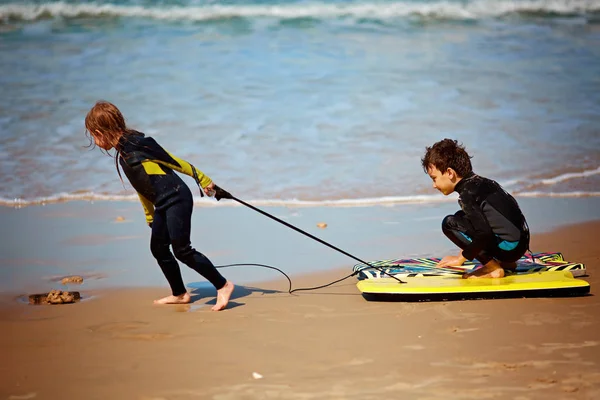 Glad bror och syster leker på stranden med en kropp-styrelse — Stockfoto