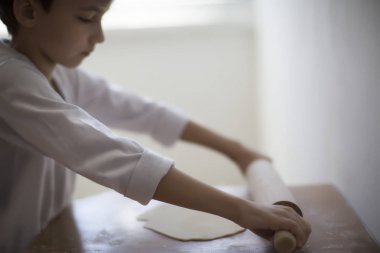 Hamur raf ile oynama ve evde mutfakta yemek yaparken gülümseyen sevimli küçük çocuk. Köfte, börek, Paskalya, pizza, pasta, yemek yaparken eğlenceli sahip çocuk evde mutfak ekmek.