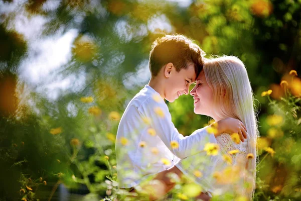 An attractive, smiling mother hugs her child in her lap while sitting outside in the grass and wild flowers — Stock Photo, Image