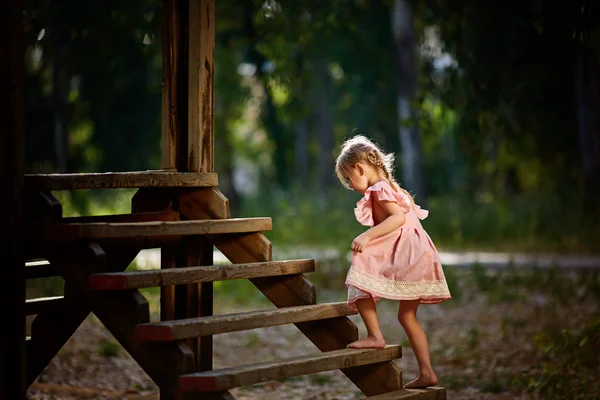 Śliczną dziewczynkę z wyrażeniami twarz zabawny gry, wspinania się na schody drewniane — Zdjęcie stockowe