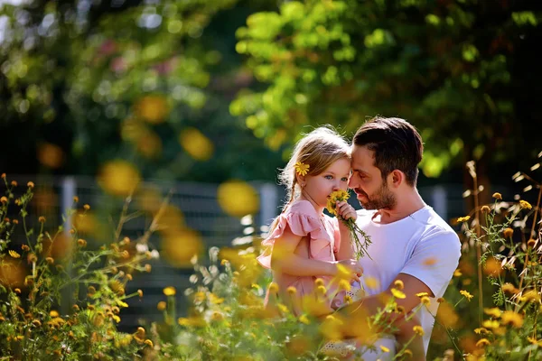 Papá y su hija juegan con flores amarillas durante el día. Concepto de familia amigable — Foto de Stock
