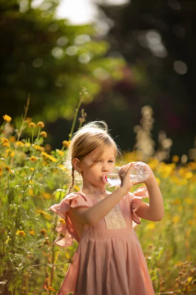 Söt liten flicka dricksvatten i en sommarträdgård — Stockfoto