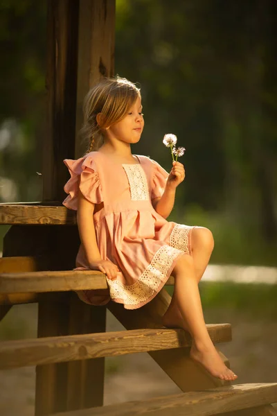 Happy small girl blowing dandelion flower outdoors. Girl having fun in spring park. — Stock Photo, Image